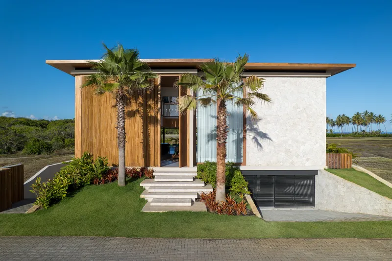 Front facade with vertical timber cladding and white stucco flanking a central entrance with palm trees