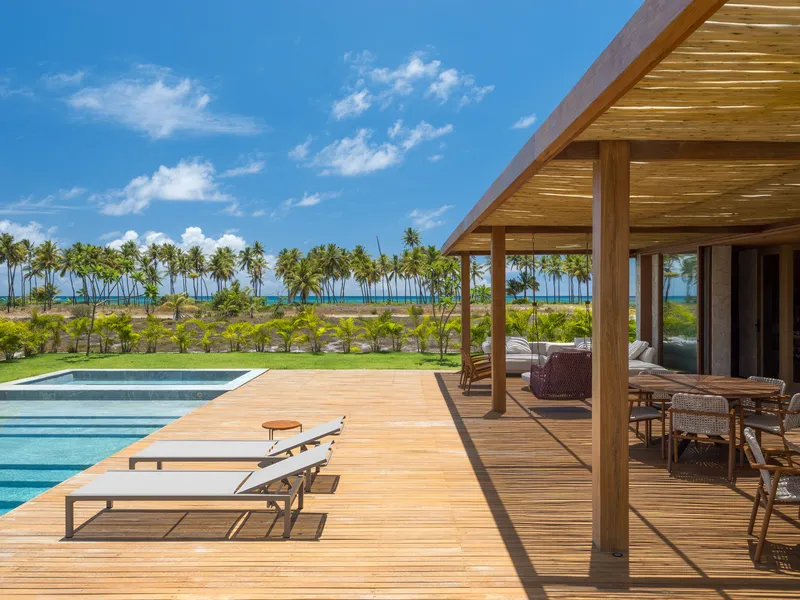 Timber deck terrace with pool and covered pergola overlooking a palm-lined coastal landscape