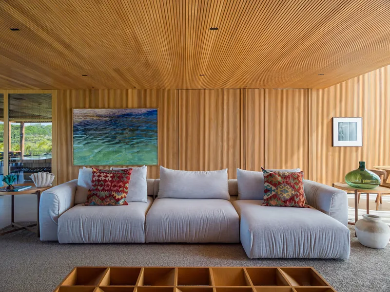 Living room with slatted timber ceiling and walls behind a sectional sofa with patterned cushions