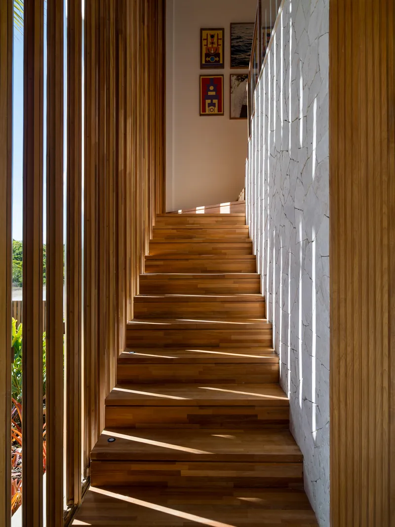 Timber staircase ascending between vertical wood slat screen and white textured wall with framed art