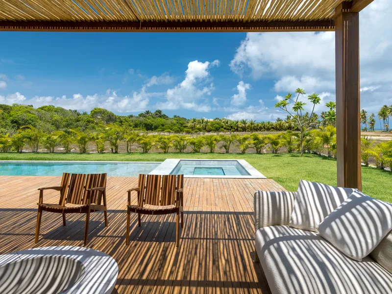 Covered terrace with timber pergola overlooking pool deck and lawn under scattered clouds