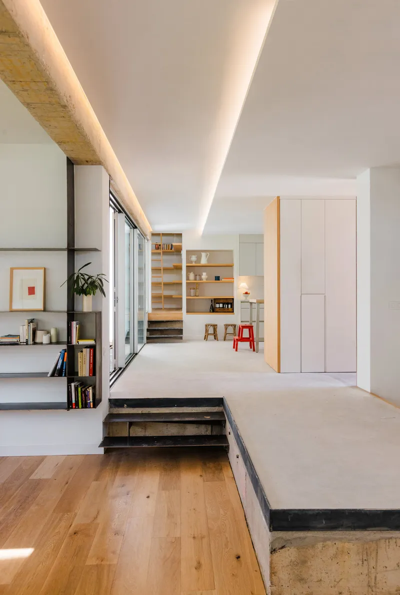 Open plan interior with recessed linear ceiling light, raised concrete platform and oak flooring