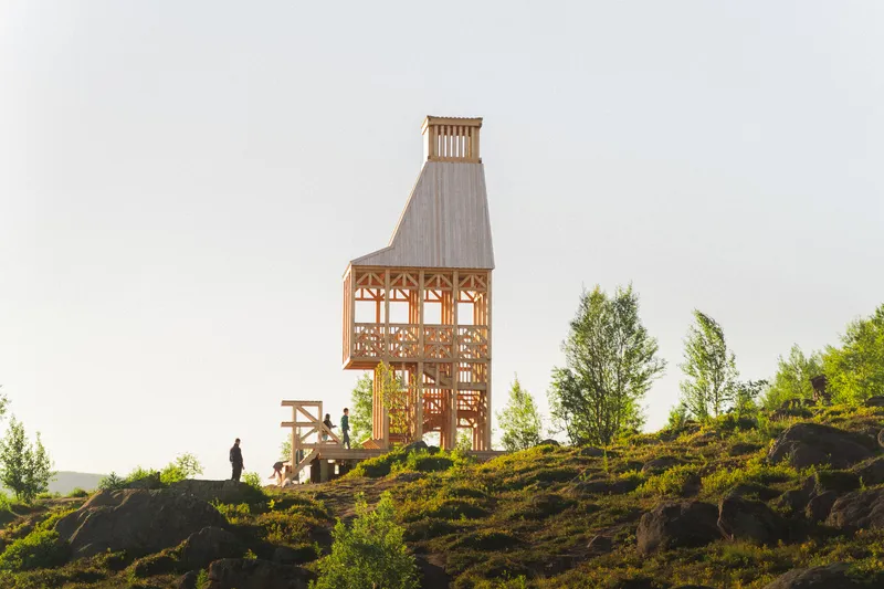 Timber observation tower with open lattice walls on a rocky hillside with visitors approaching at dusk