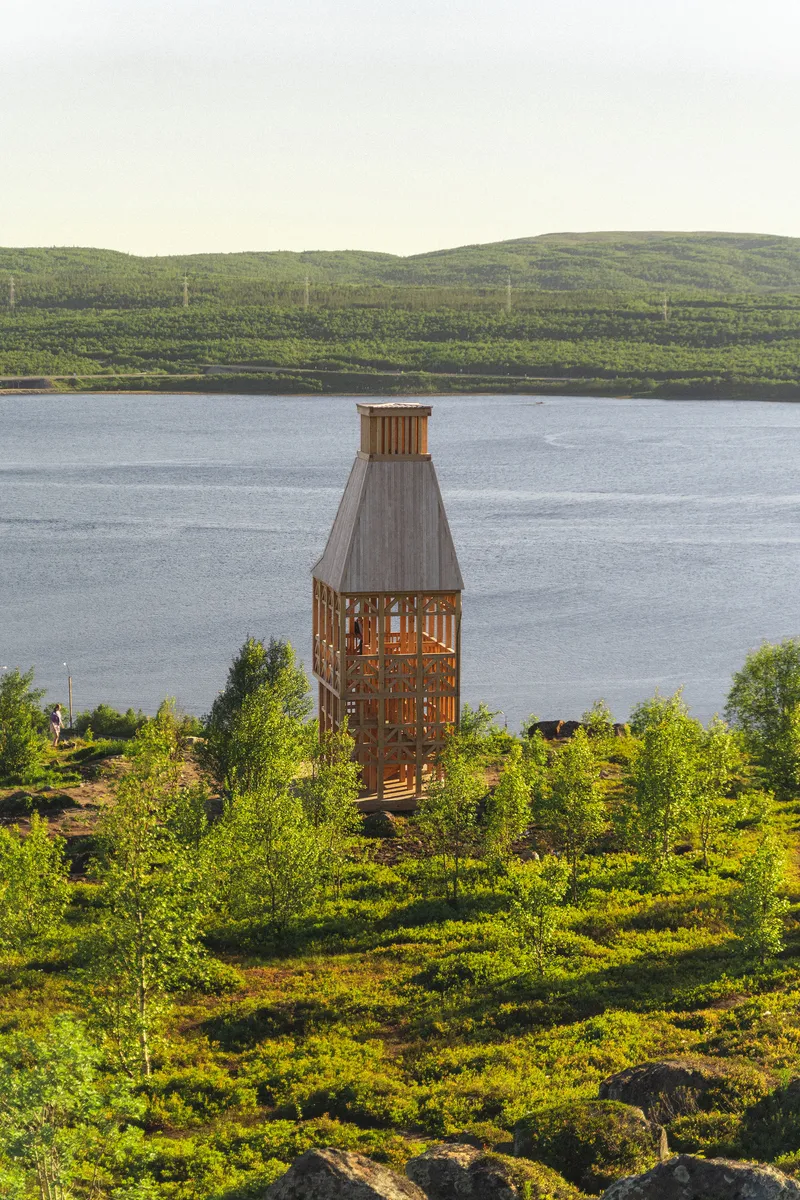 Timber lookout tower on vegetated slope overlooking calm lake and forested hillside in afternoon light