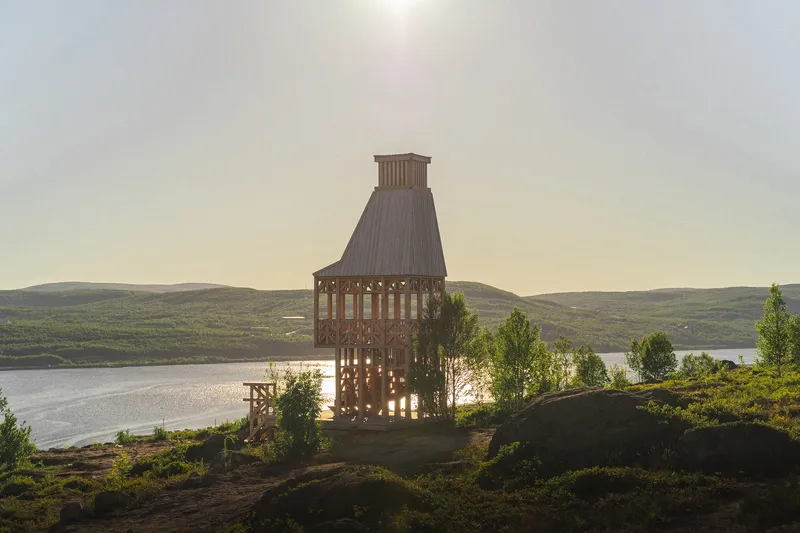 Timber frame tower with latticed walls silhouetted at sunset above a rocky coastal landscape