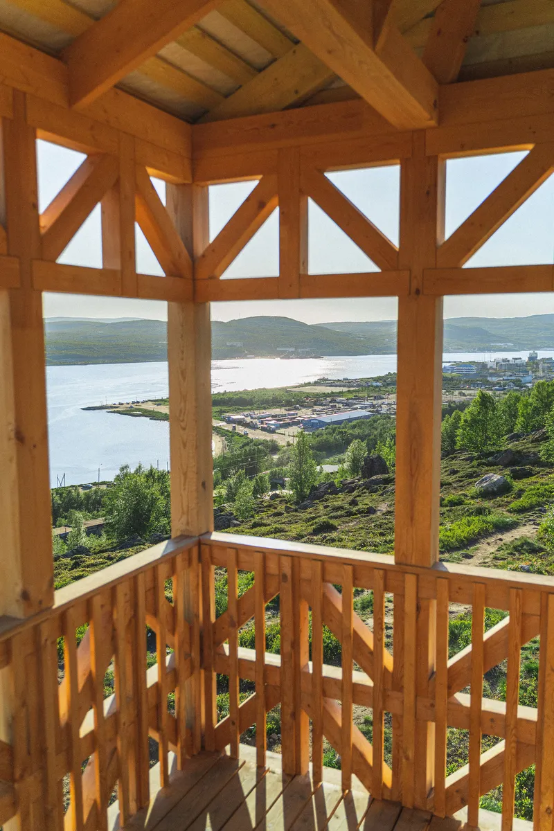 Timber belvedere with patterned screen railings overlooking a fjord and distant hills in summer