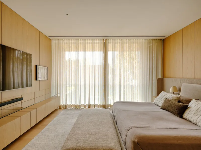 Bedroom with floor-to-ceiling sheer curtains filtering soft daylight and timber millwork built into the walls