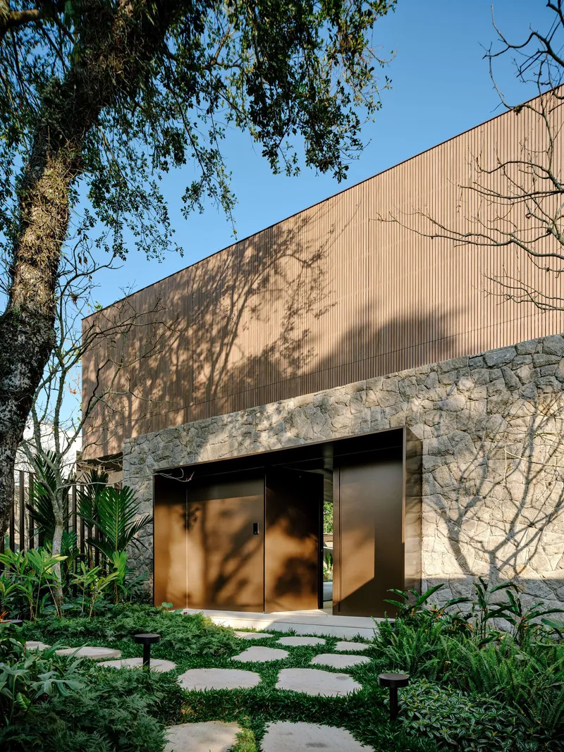 Stone base and vertical timber cladding facade with bronze entry doors framed by stepping stone path