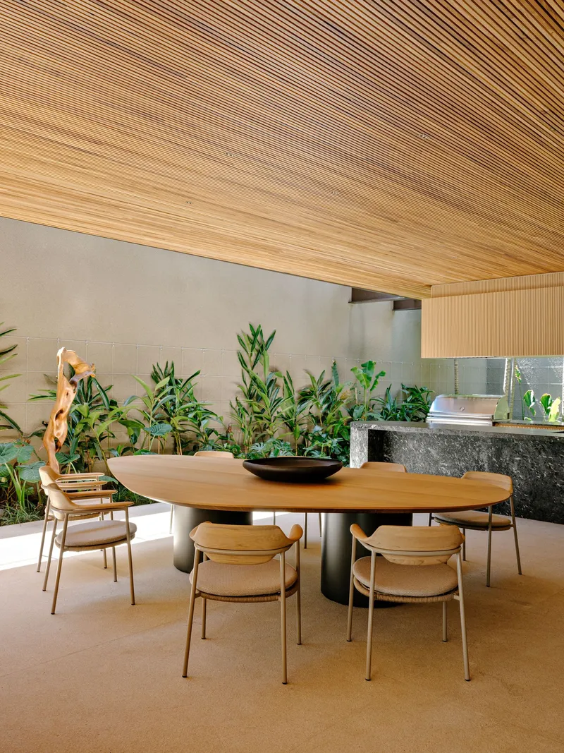 Dining area with timber slat ceiling above an oval table and planted bed along the wall