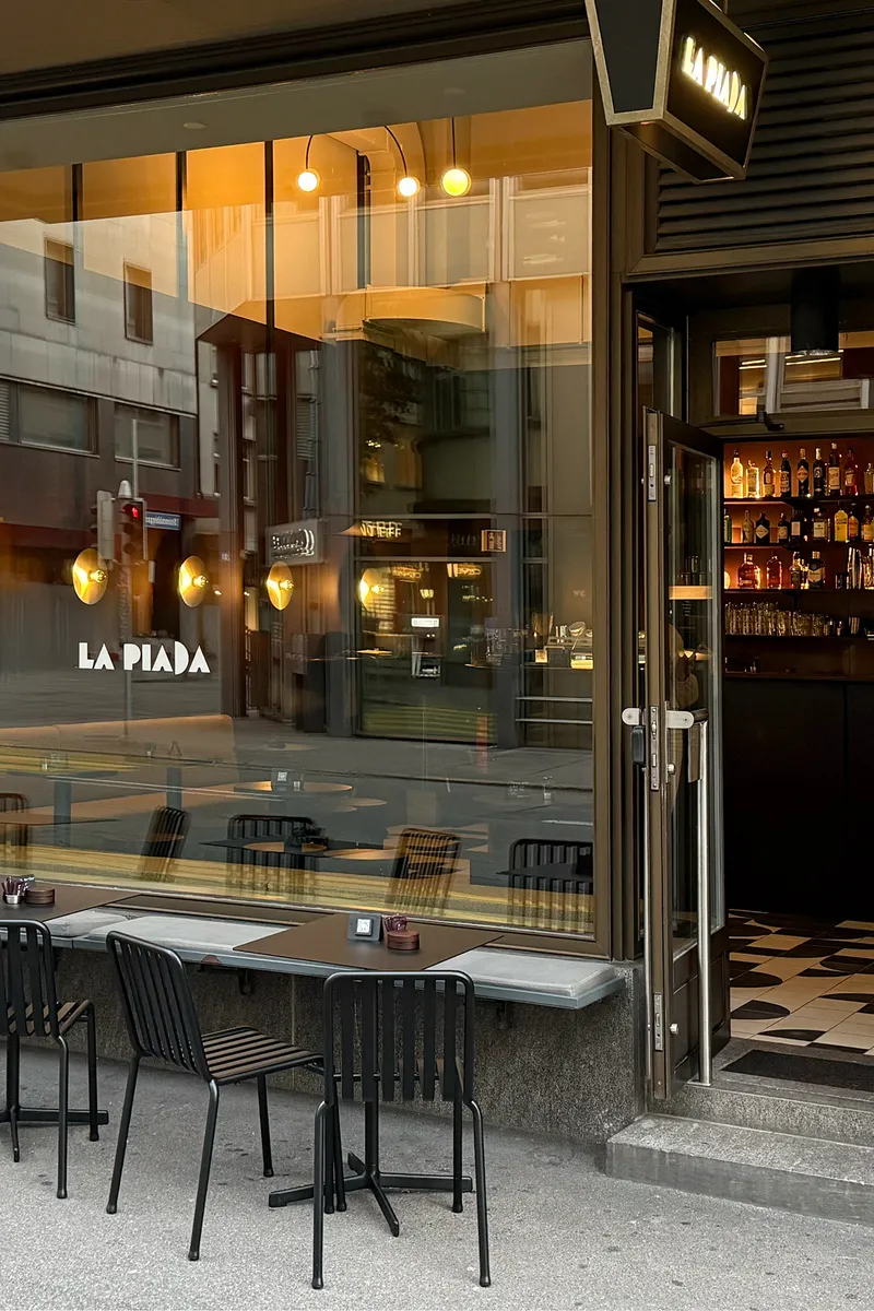 Street-facing glazed facade with open door revealing interior bar at dusk