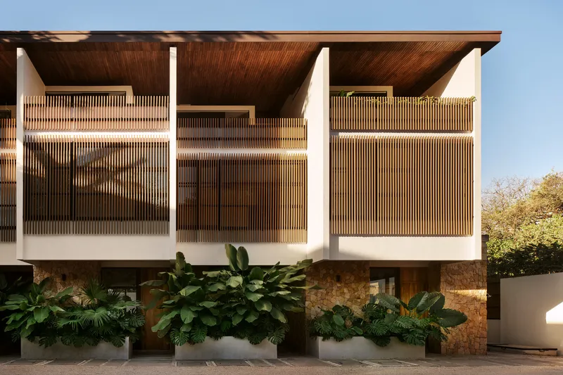 Elevated facade with vertical timber louvers and planted beds with tropical foliage at ground level