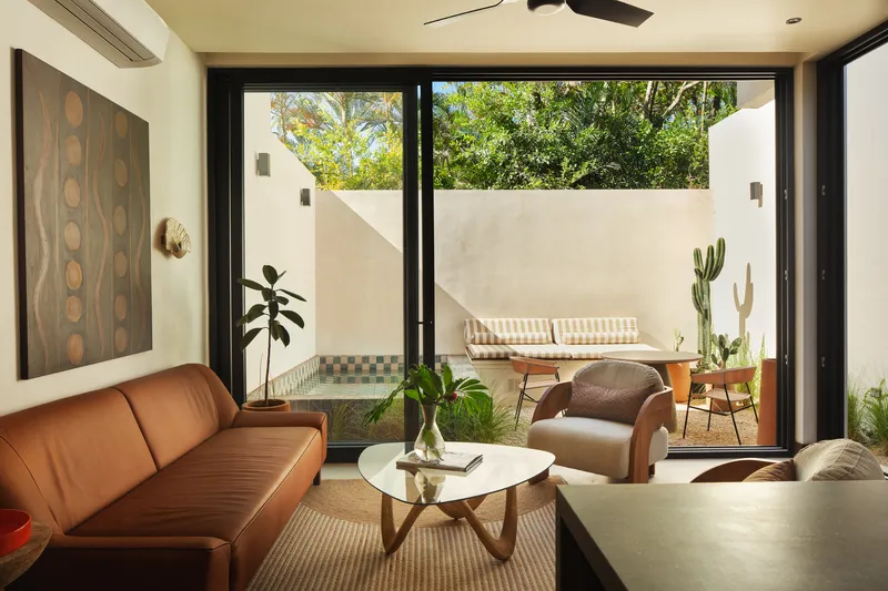 Living room opening to a walled terrace with tiled fountain and outdoor furniture beneath afternoon sun