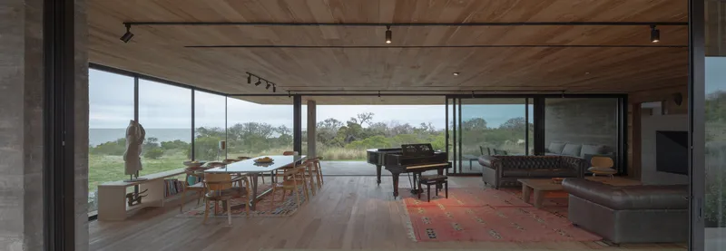 Open-plan living space with timber ceiling, floor-to-ceiling glass, and views to the landscape beyond