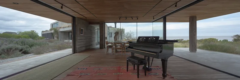 Covered terrace with timber columns framing the living area and a grand piano under cloudy skies