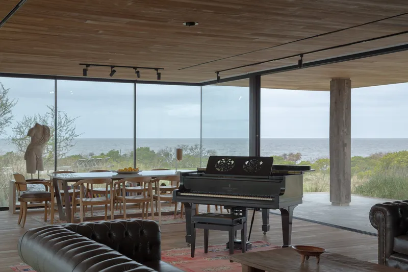 Dining and living area with glazed walls opening to the ocean horizon under diffused daylight