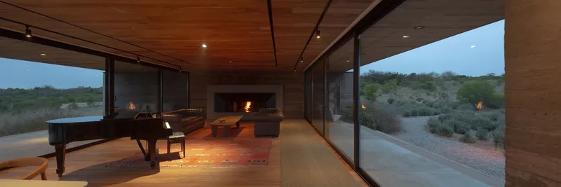 Living room with timber ceiling and floor-to-ceiling glass opening to desert landscape at dusk