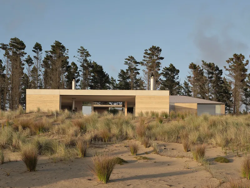 Horizontal timber-paneled volumes with central glazed opening backed by tall pine trees at dusk