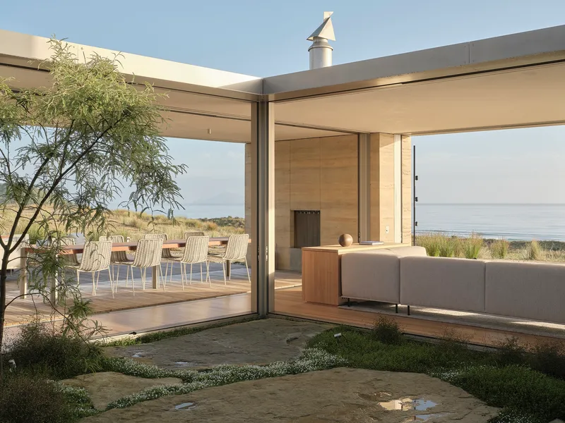 View through sliding glass doors to timber deck and outdoor seating area overlooking coastal landscape