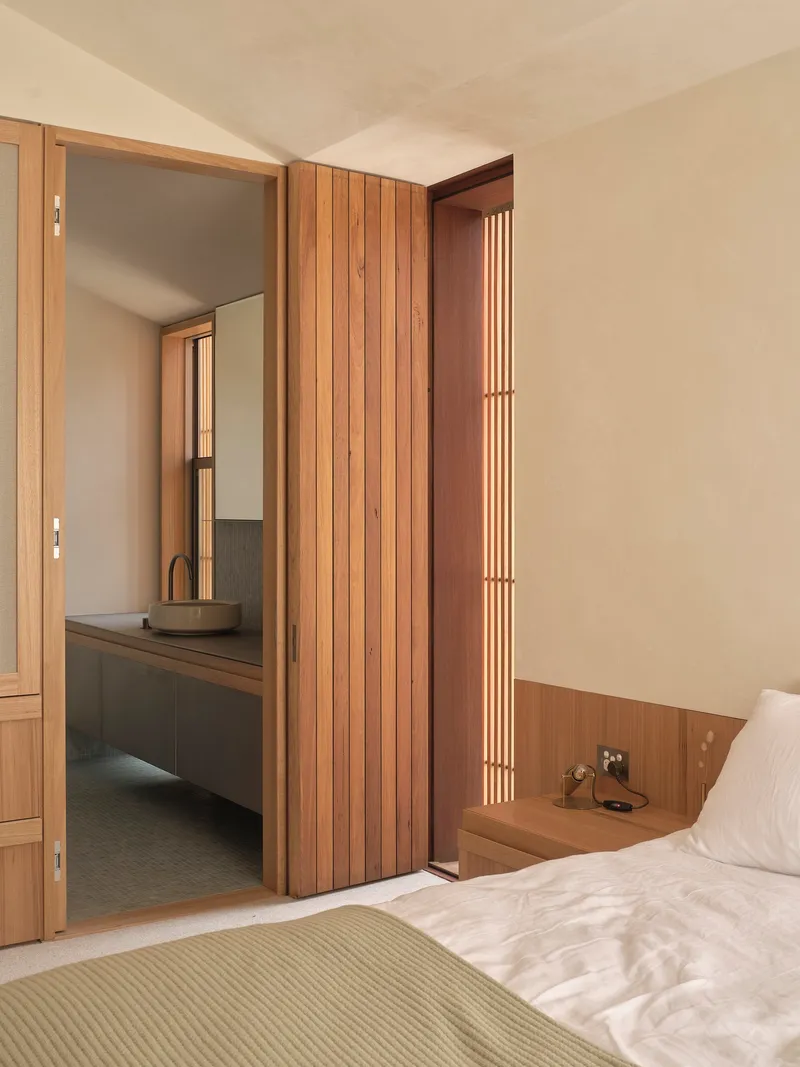 Bedroom view through timber-clad doorway to ensuite bathroom with floating vanity and vertical slatted window