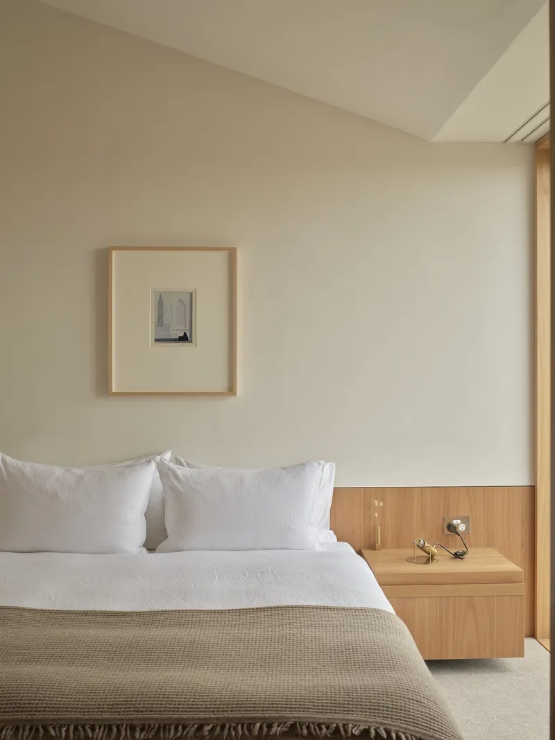 Bedroom with integrated timber bedside shelf and framed artwork on pale plaster wall