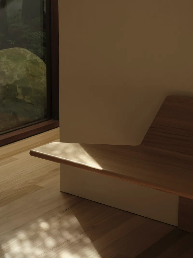Built-in timber bench with cream plinth beside a floor-to-ceiling window in dappled afternoon light