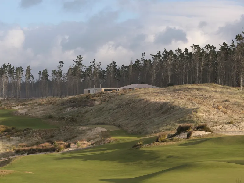 Low horizontal structure on a hillside overlooking a golf course with pine forest beyond