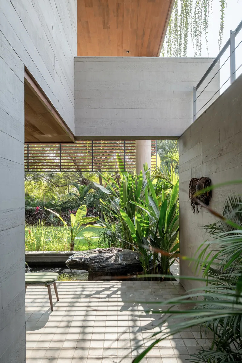 Narrow courtyard passage with board-formed concrete walls, timber ceiling soffit and planted reflecting pool