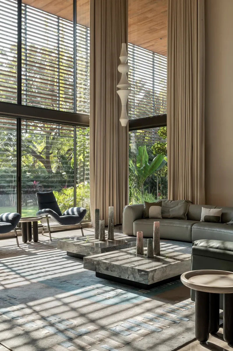 Double-height living room with horizontal louvered windows casting striped shadows across polished floor