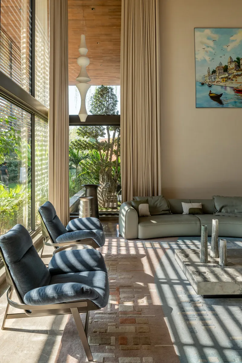 Living room with double-height windows casting horizontal louver shadows across the terracotta floor