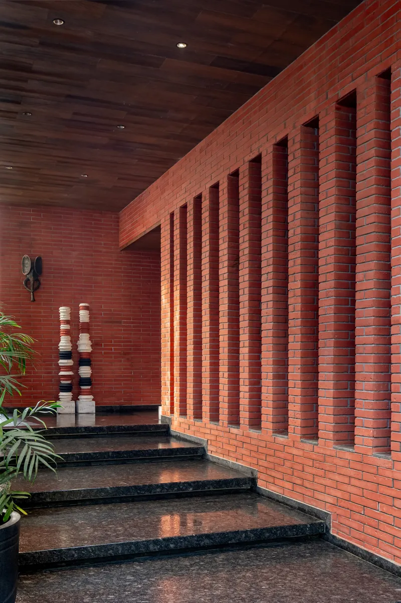 Interior staircase with terrazzo treads rising past a red brick wall with vertical recessed channels