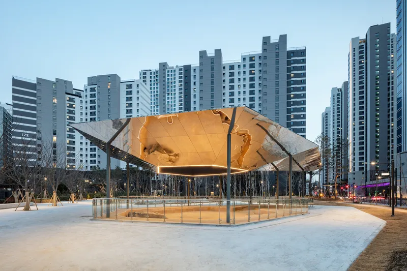 Elevated hexagonal canopy with illuminated copper-toned underside above a glass-enclosed plaza at dusk