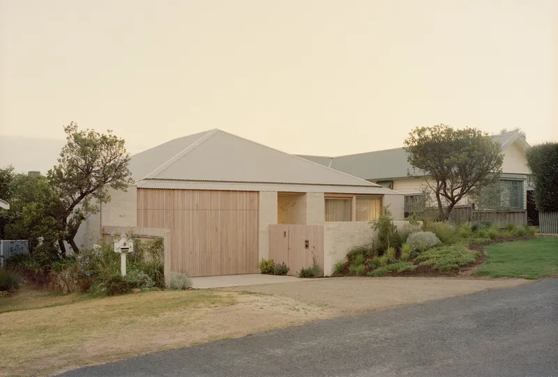 Street view of the sandstone and timber facade with gabled corrugated metal roof under hazy skies