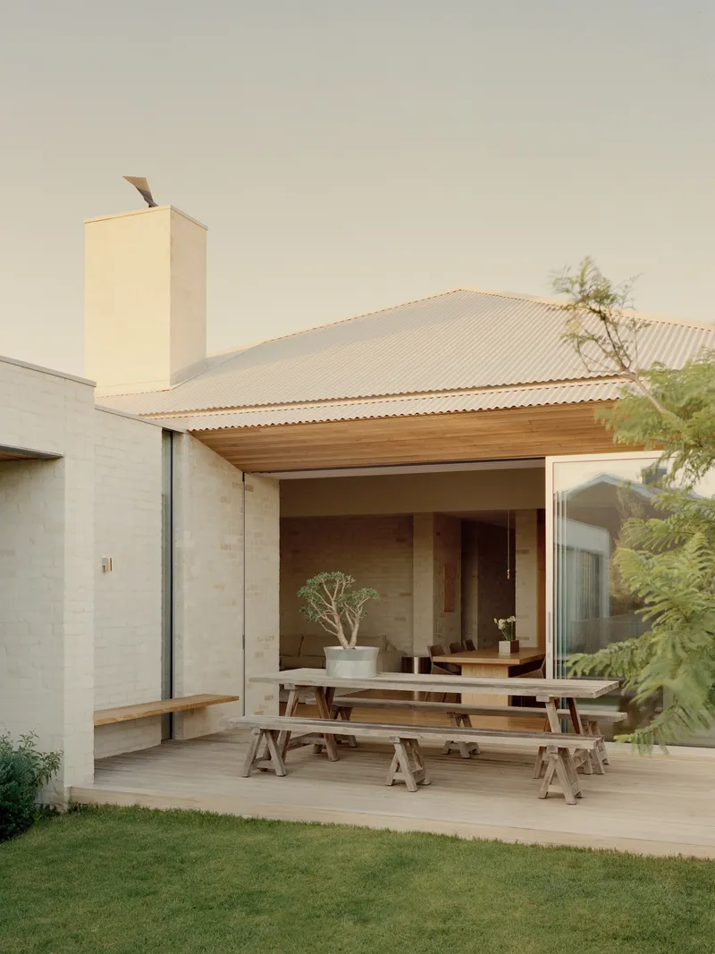 Covered terrace with timber benches extending from the glass doors beneath the corrugated overhang