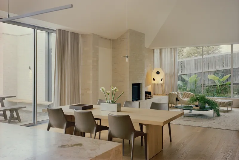 Open-plan living and dining space with rammed earth walls and floor-to-ceiling glass overlooking the garden
