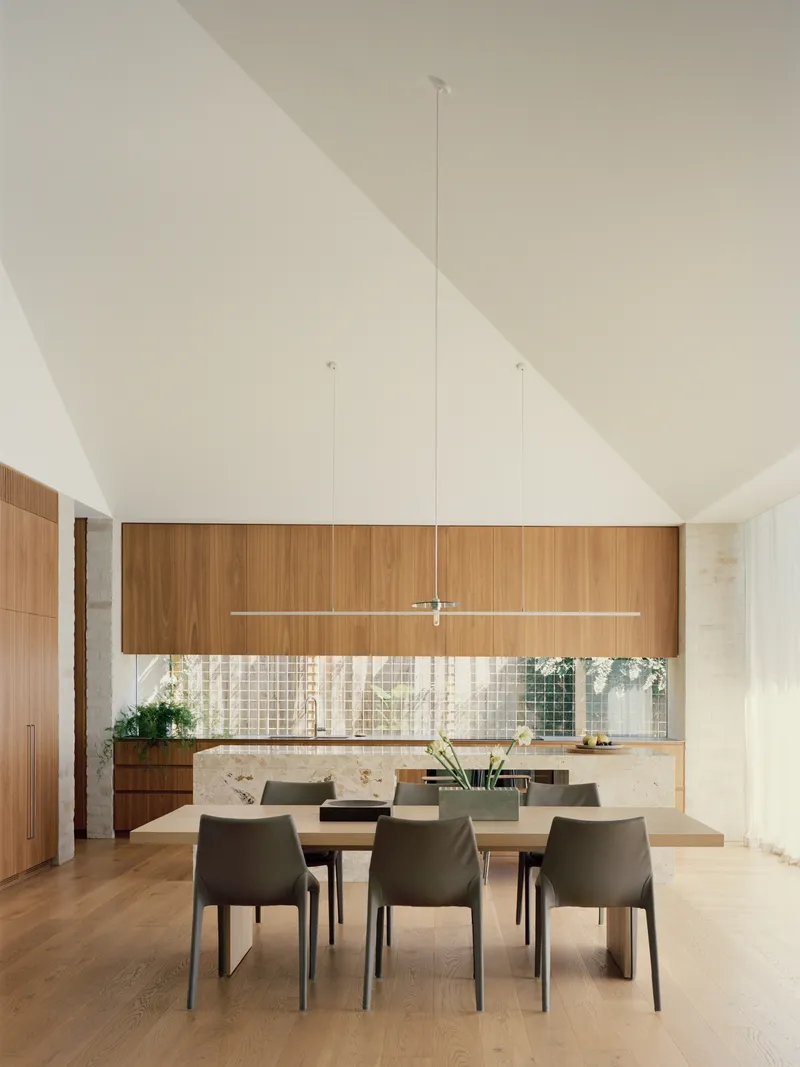 Dining area beneath vaulted ceiling with timber cabinetry and mosaic tile backsplash in soft daylight
