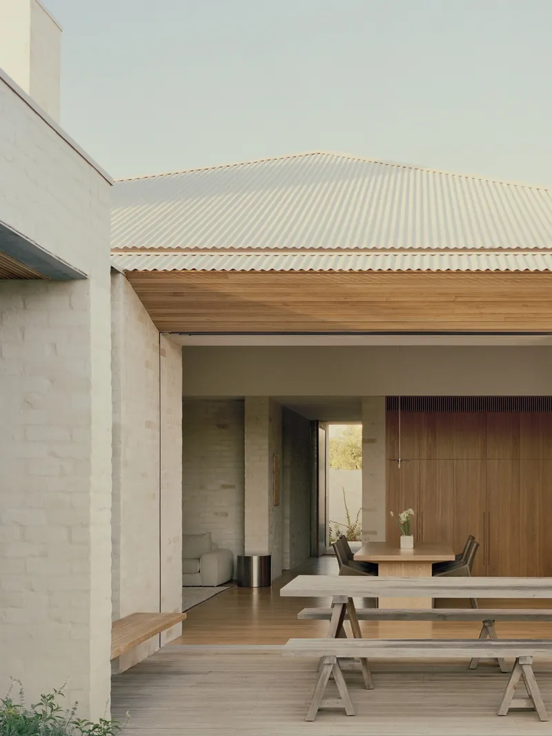 Covered outdoor dining area with timber benches under the corrugated roof looking into the interior