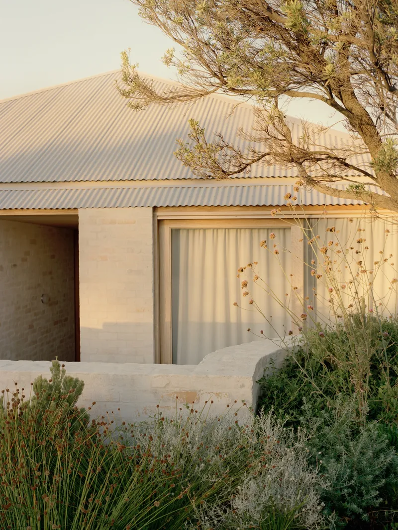 Facade detail showing limestone base and corrugated metal roof with windswept tree overhead