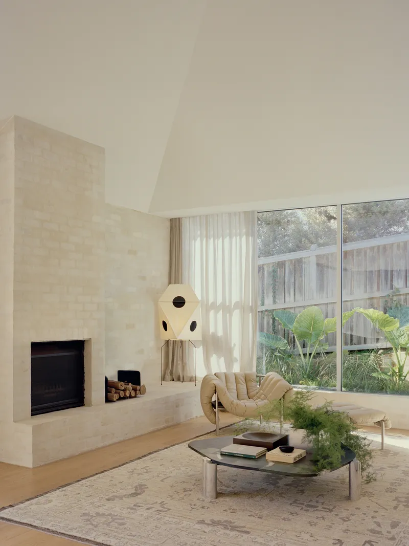 Living room with limestone fireplace wall and floor-to-ceiling windows overlooking planted courtyard