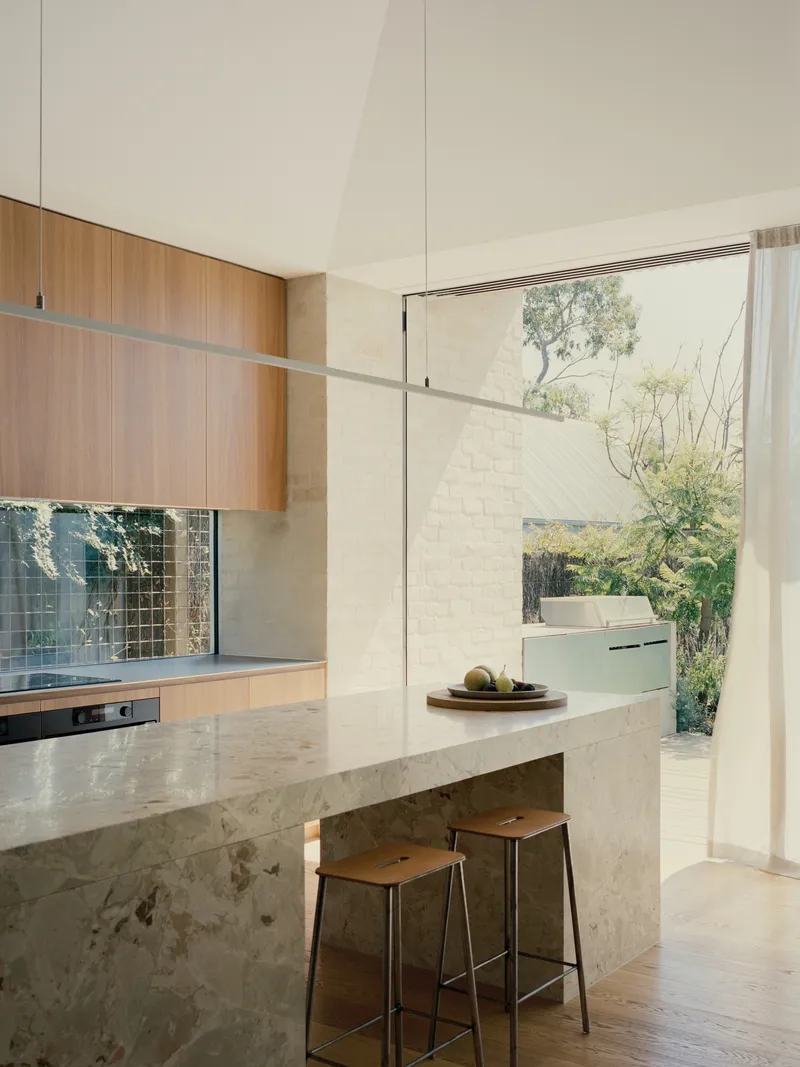 Kitchen island in mottled stone with timber cabinetry and glass doors opening to courtyard