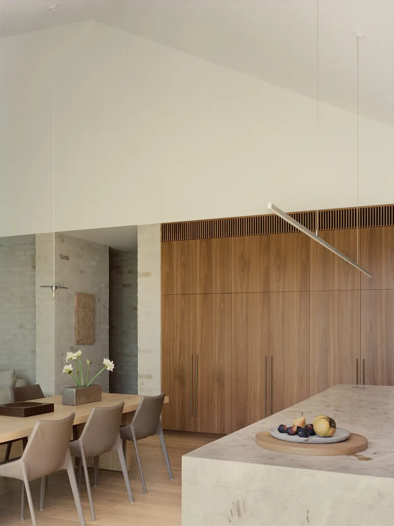Open dining area with timber storage wall and suspended linear pendant above stone island