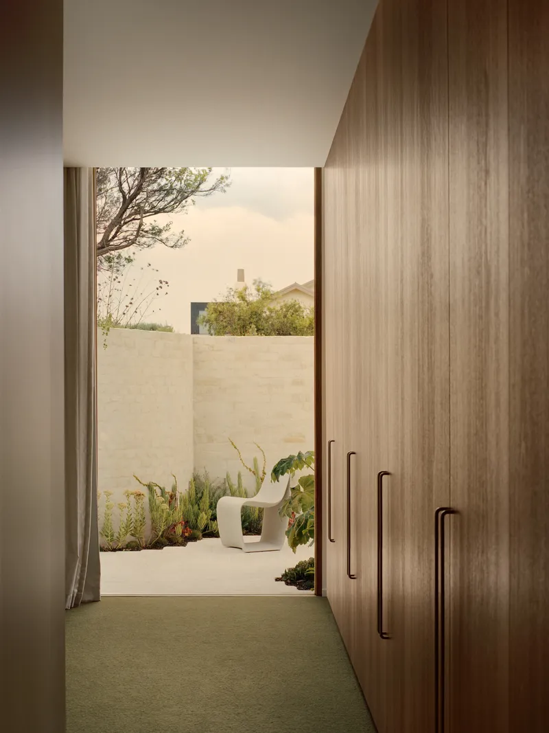 Hallway with timber joinery leading to planted courtyard with limestone walls