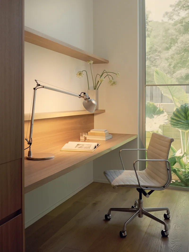 Built-in timber desk with task lamp beside a full-height window overlooking tropical planting
