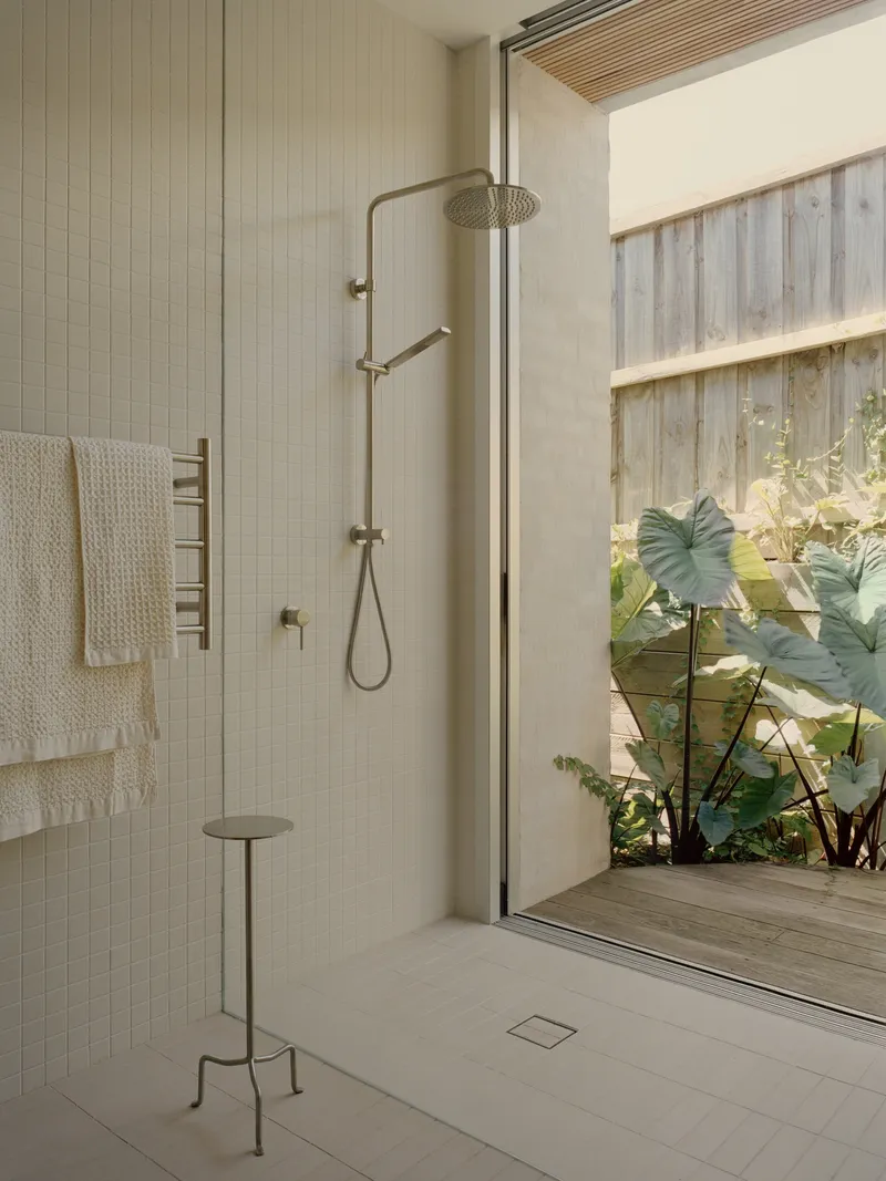 Walk-in shower with brass fixtures opening onto a private garden courtyard through sliding glass doors