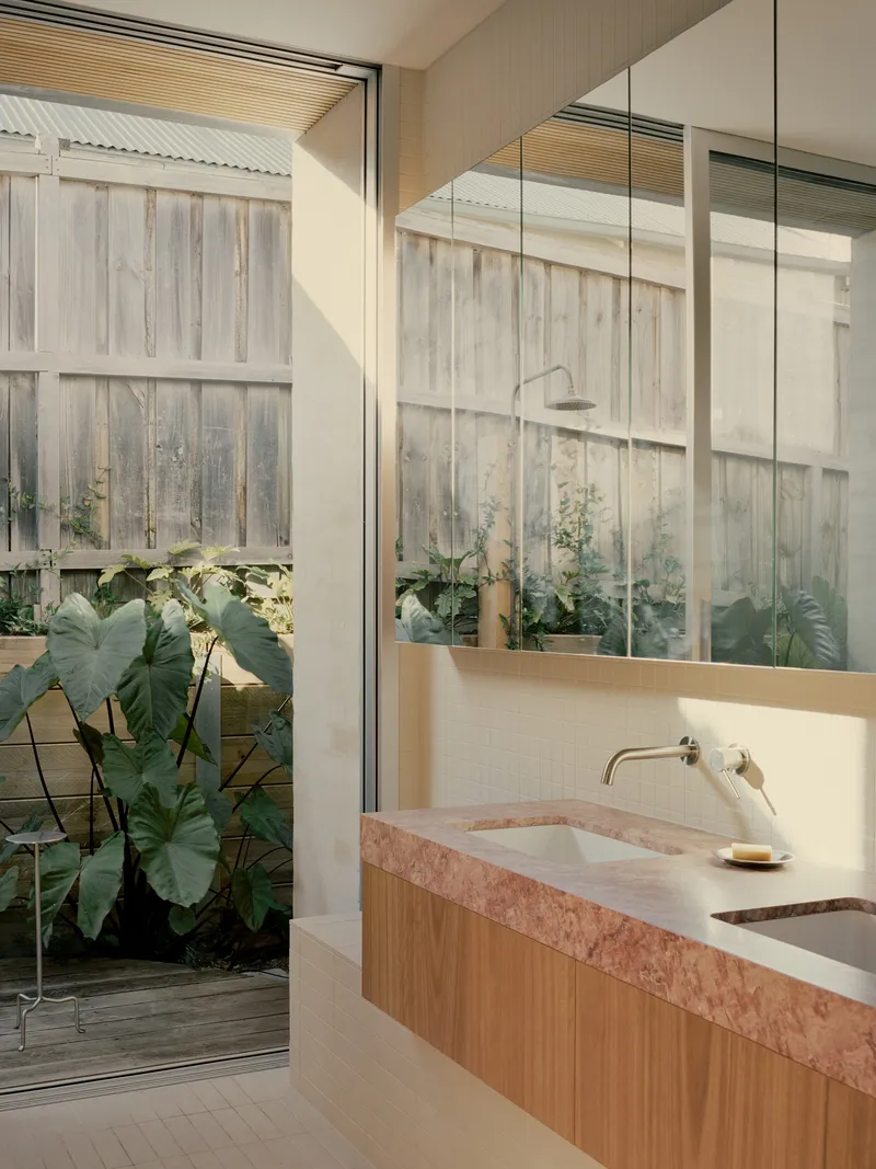 Pink stone vanity counter beside open glazed doors revealing weathered timber fence and plantings