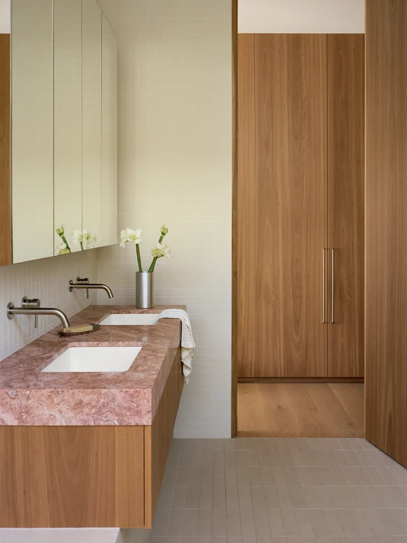 Double vanity with pink stone countertop and white tile backsplash adjacent to timber wardrobe doors