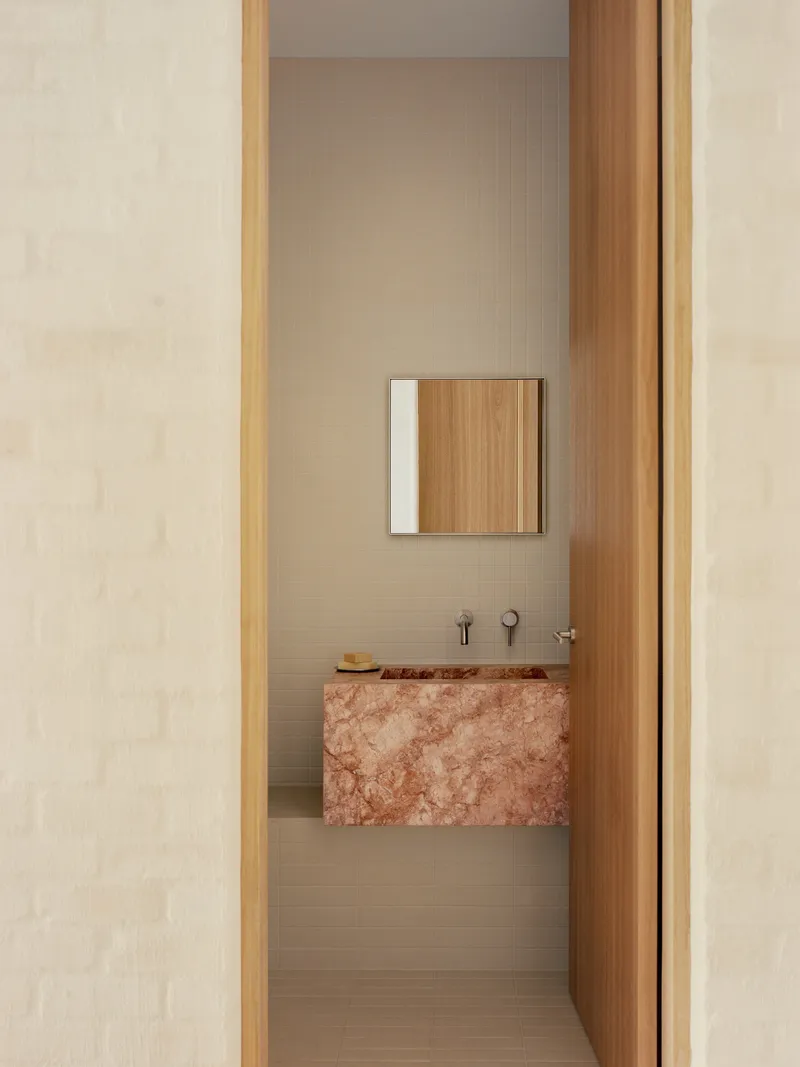 View through timber doorway to a powder room with cantilevered pink stone basin