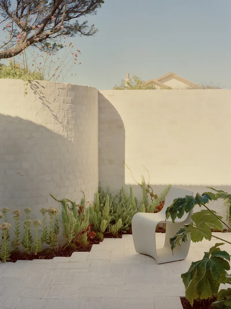 Terraced courtyard with curved stucco walls, planted beds of grasses and cacti, and a white sculptural seat