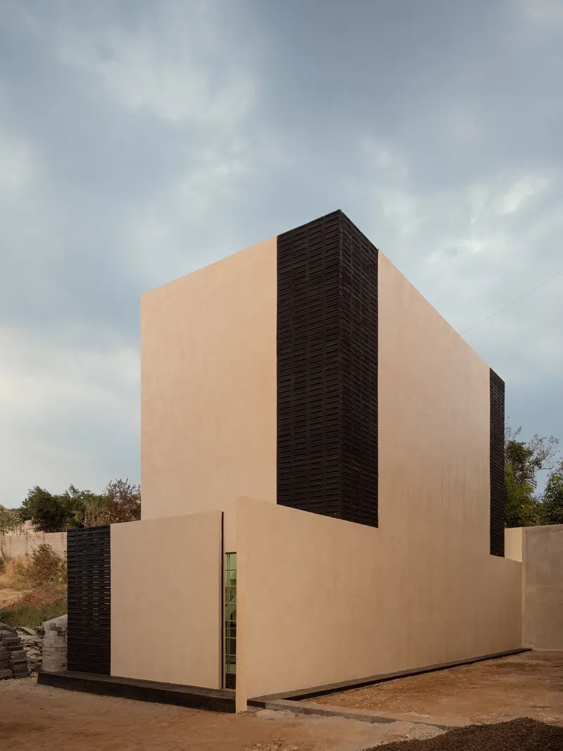 Two-story volume clad in smooth plaster and horizontal louvers under an overcast sky