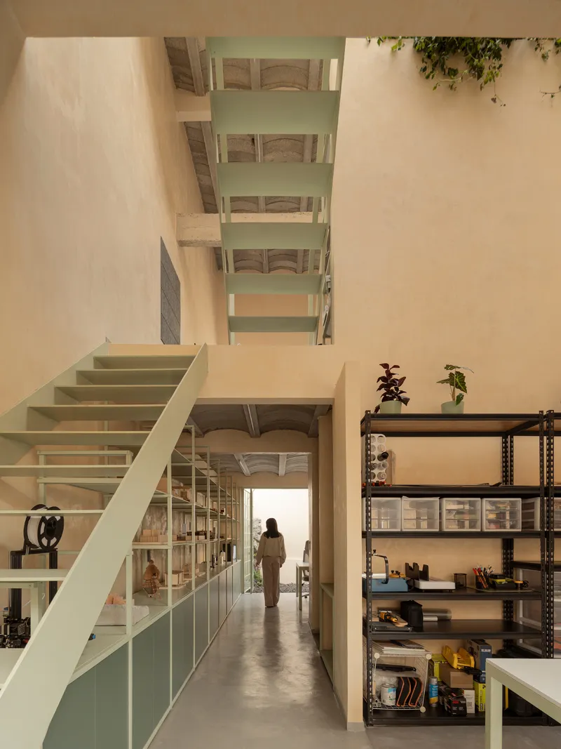 Interior hallway with pale green staircase rising to a skylight above a person walking toward sunlit entry