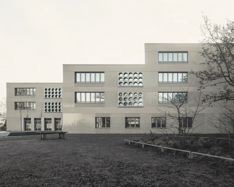 Stepped facade with alternating rectangular windows and circular perforated panels in pale brick under an overcast sky